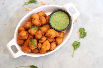 Moong dal ke pakode, ram laddoo, bhajias, Moongode or fritters. served with green mint and coriander chutney. Served over light background. Selective focus. with copy space.