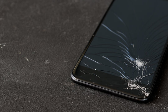 Broken glass of black smart phone on the dark background. Selective focus. Copy space