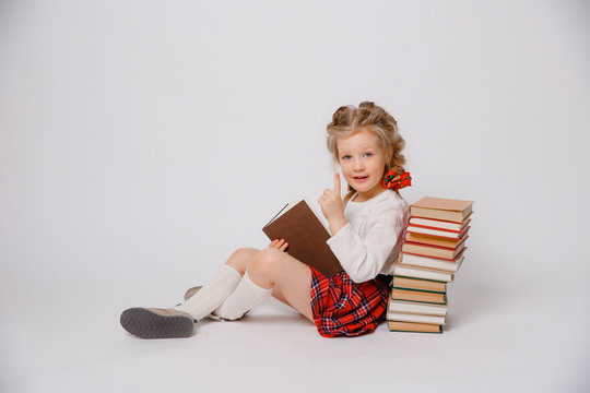 child girl in school uniform with a book in her hands sitting isolated on a white background