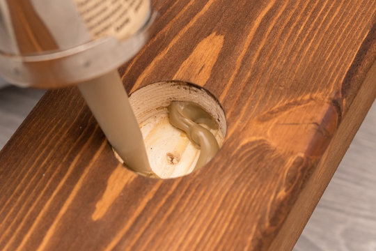 The mounting glue is extruded into a drilled round hole in a wooden board