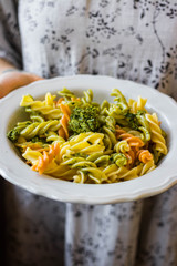 Woman hold vegan pasta in hands, colorful macaroni with vegetables on plate. Mediterranean Italian traditional healthy food on lunch or vegetarian dinner.