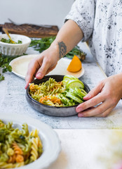 Woman serve vegan pasta on table, colorful macaroni with vegetables on plate. Mediterranean Italian traditional healthy food on lunch or vegetarian dinner.