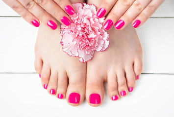 Pink manicure and pedicure with a flower on white wooden background, top view.
