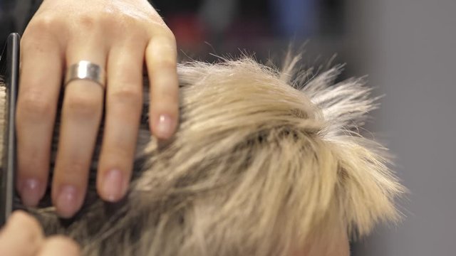 A stylist in a hair salon checks the regrown hair roots of a blonde girl
