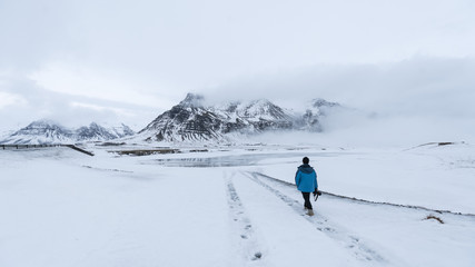 Fototapeta na wymiar A man walking on the snow field with mountain at background, Iceland