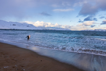 Teriberka, Murmansk region / Russia - 02.19/2020: Coast of the Arctic ocean. Surfer comes out of the icy ocean water