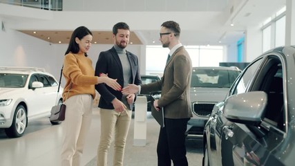 Slow motion of young couple man and woman buying car shaking hands with agent hugging taking keys enjoying successful deal. People and shopping concept. - Powered by Adobe