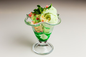 Pistachio ice-cream with candied fruits and green syrup, garnished with mint, served in a transparent glass vase