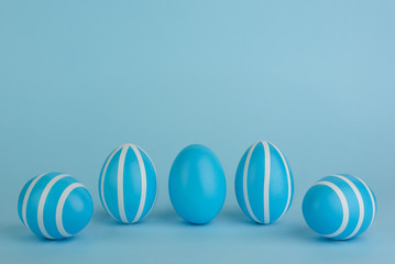 Easter decorated blue eggs. Five striped blue eggs in a row on a blue background. White stripes stripes. Monochrome concept. Copy space. Happy Easter card.