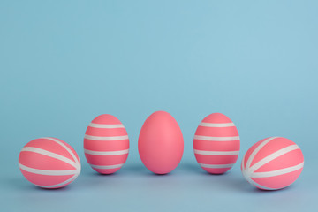 Fototapeta na wymiar Easter decorated pink eggs. Five striped pink eggs in a row on a blue background. White stripes on pink painted eggs. Copy space. Happy Easter card. Colourful Easter concept.