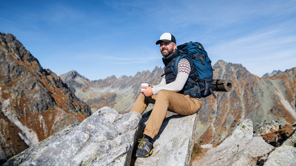 Mature man with backpack hiking in mountains in autumn, resting.