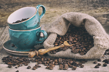 Coffee cup with coffee beans in burlap sack on wooden table, selective focus with  shallow depth of field
