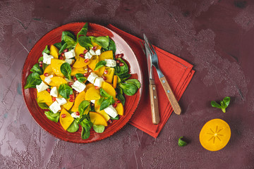 Healthy salad with persimmon, doucette (lambs-lettuce, cornsalad, feld salad) and feta cheese. Fitness food, superfoods vitamin persimmon salad. Top view, flat lay, copy space.