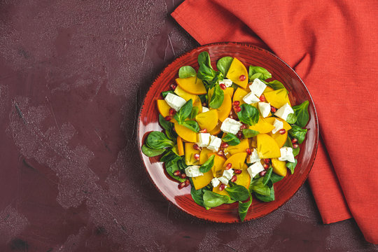 Healthy salad with persimmon, doucette (lambs-lettuce, cornsalad, feld salad) and feta cheese. Fitness food, superfoods vitamin persimmon salad. Top view, flat lay, copy space.