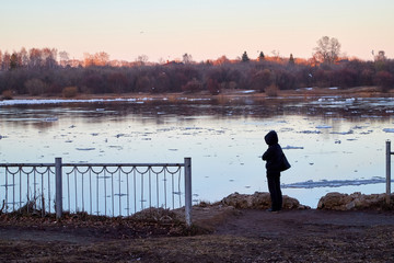 Ice drift on the river and girl watching it from high coast in the evening at sunset in the Northern part of Russia