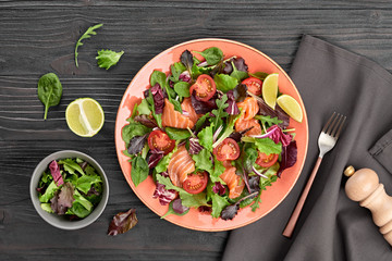 Salmon salad with cherry tomatoes, spinach, radicio, lollo on dish. Healthy seafood, salmon fish, creative diet concept. Tasty salmon and mixed leaves salad on dark wood, flat lay