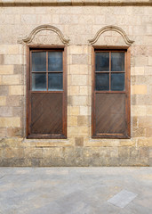 Facade of old abandoned stone decorated bricks wall with two adjacent arched wooden shutter windows 