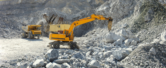 Hydraulic breaker hammer in a quarry for limestone mining with an excavator and a quarry truck in...