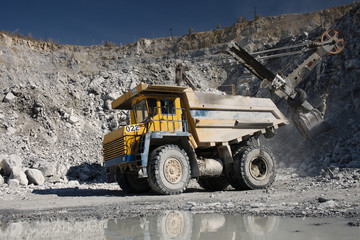 Large quarry dump truck on the background of a working excavator in a limestone quarry, close-up. Heavy equipment.