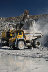 Excavator during the loading of rock ore into the body of a heavy duty dump truck in a limestone quarry, close-up. Heavy equipment.
