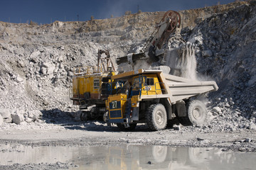 Heavy quarry dump truck and a heavy quarry excavator during loading in a quarry for limestone mining, close-up. Heavy equipment.