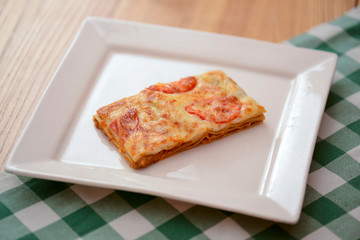 Small piece of tomato lasagna on a square white plate. Dinner in a restaurant, cafe or diner. Healthy food concept.