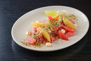 Citrus salad with smoked salted salmon fish, grapefruit, orange, sesame seeds and spices served on white plate