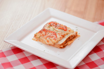 Small piece of tomato lasagna on a square white plate. Dinner in a restaurant, cafe or diner. Healthy food concept.