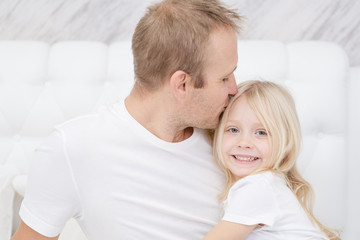 Close-up shot of young father kissing little smiling daughter. Sincere parents love