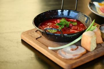 Traditional Ukrainian Russian vegetable borscht served in a black bowl on the old wooden background.