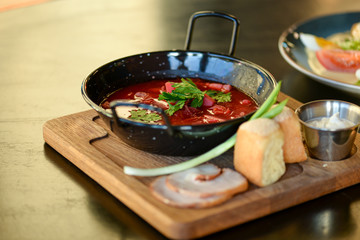 Traditional Ukrainian Russian vegetable borscht served in a black bowl on the old wooden background.