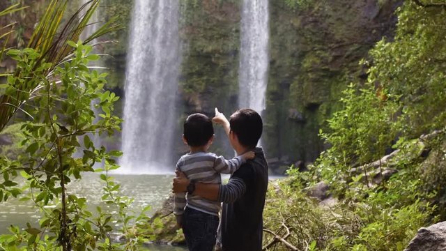 Slowmotion video of asian father and son visiting a tropical waterfall
