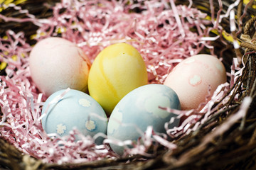 Fototapeta na wymiar A nest of twigs and hay and a pink paper filler with pastel colored Easter eggs. Colored eggs for the holiday of light Easter. Easter card on a yellow background