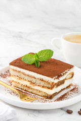 Tiramisu. A slice of a traditional Italian dessert on a white plate and a cup of coffee on a marble...
