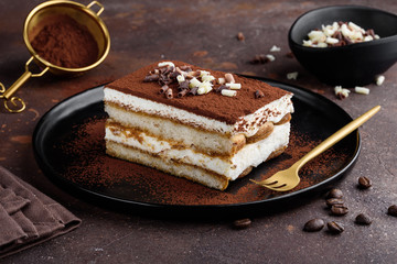 Tiramisu dessert decorated with cocoa and white and dark chocolate on a black plate. Selective focus