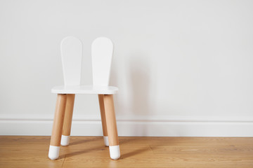 White and wooden child chair with rabbit ears. White wall copy space
