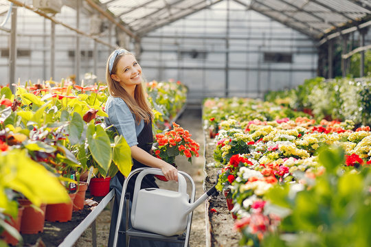 Woman in a greenhouse. Worker pours flowerpoots. Girl in a black apron.