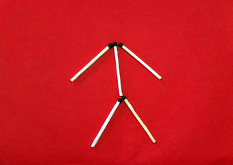 The figure and icon of a man is laid out of matches on a red background. The symbol of man of the matches. Creative and original symbol.