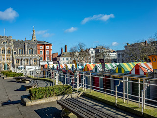 A view across a city centre market square and its colourful outdoor market stalls on a bright and sunny day