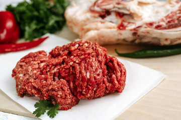 Red fresh minced meat on the background of lamb legs, red pepper and greens. Ground beef on the background of fresh meat in the kitchen of a housewife