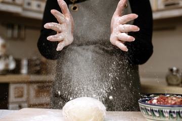 A woman prepares dough at home and claps her hands with flour. Flour scatters the housewife's kitchen