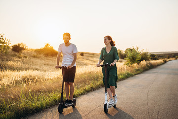 Young couple on vacation having fun driving electric scooter on the road in the countryside....