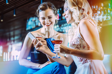 Two women in a bar looking at their mobile phone