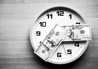 Analog clock and dollars on a wooden background. Banknotes are lying on the clock in the form of arrows. 100 dollars indicate hours and minutes. View from above. On the clock  time 20:15, 08:15