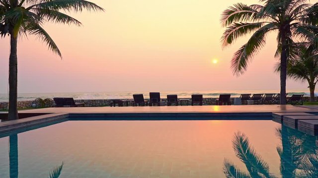 Summertime: beautiful view of the sunset at the hotel pool area line of Beach deck chairs on the beach in the foreground. Sunlight  and coconut palms reflections in pool water