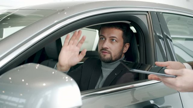 Car buyer handsome bearded man is talking to dealer in dealership inside shiny new car taking key fob ready for test drive. Business and transport concept.
