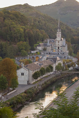 Lourdes landmark in the evening haze filtered. Cathedral of Our Lady of Lourdes with river and mountains. Famous pilgrimage centre. Rosary and sanctuary in Lourdes, France. Religious architecture.