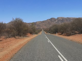 Straße durch die Wüste mit Dornensträuchern und Bergen, Australien