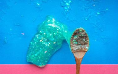 Transparent slime with sequins and oxygen bubbles flows down from a wooden spoon on a blue background with a pink stripe for the inscription. - Powered by Adobe
