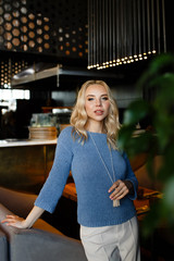 Business portrait of an attractive beautiful blonde woman in a blue jacket and white trousers in a cafe restaurant, a girl working , drinking coffee, talking on the phone, freelancing